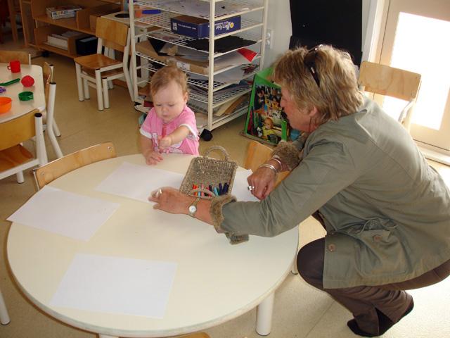 Adult and toddler holding a pen with 3 pieces of paper on a round table