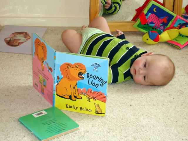 Baby lying on the floor in front of a book called Roaring Lion by Emily Bolam