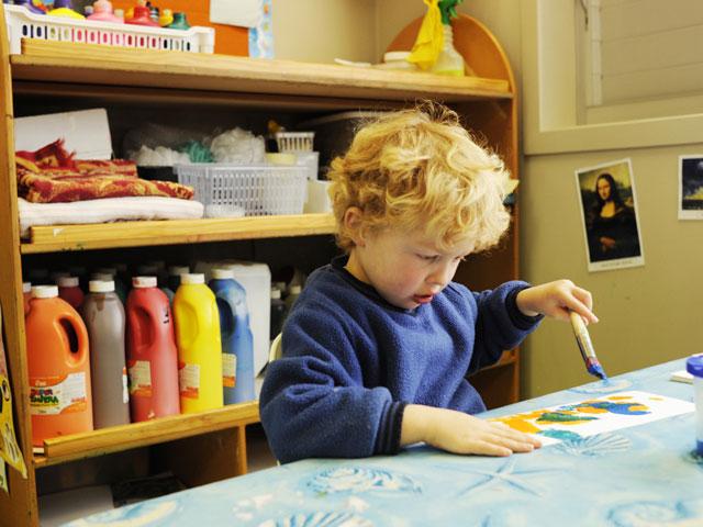 Boy painting with storage shelves in background for art materials